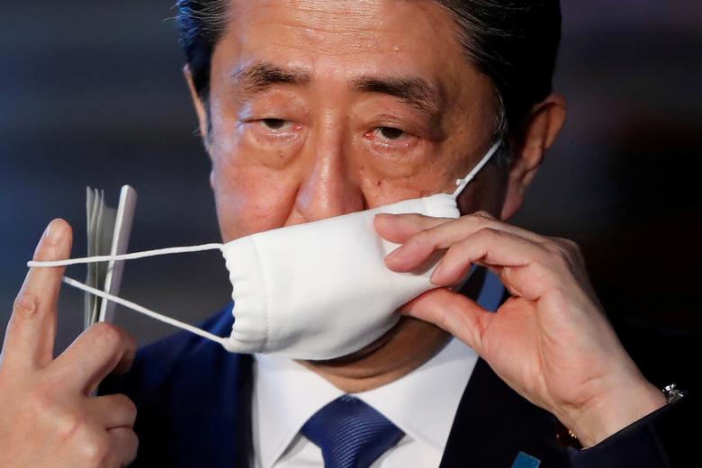 Япония бош вазири Синдзо Абэ мамлакатда коронавирусга қарши курашда амалга оширилаётган ишлар бўйича журналистларга маълумот бериш олдидан ниқобини ечмоқда.
