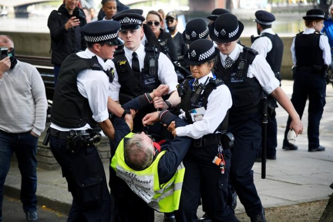 Лондонда полиция ходимлари карантин қоидаларига қарши намойишга чиққанлардан бирини кўтариб олиб кетмоқда.