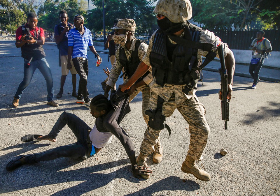 Гаити пойтахтидаги ҳукуматга қарши намойишда иштирокчини судраб кетаётган полициячи.