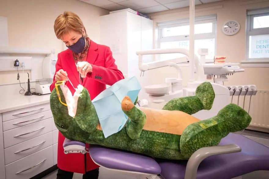 Шотландия биринчи (бош) вазири Никола Стержен сайловолди ташвиқоти пайтида Thornliebank Dental Care клиникасига ташрифи давомида ўйинчоқ динозаврларнинг тишларини текширмоқда.
