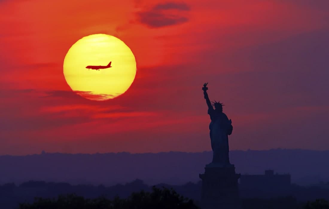 Нью-Йоркда қуёш ботиши фонидаги самолёт ва Озодлик ҳайкали.