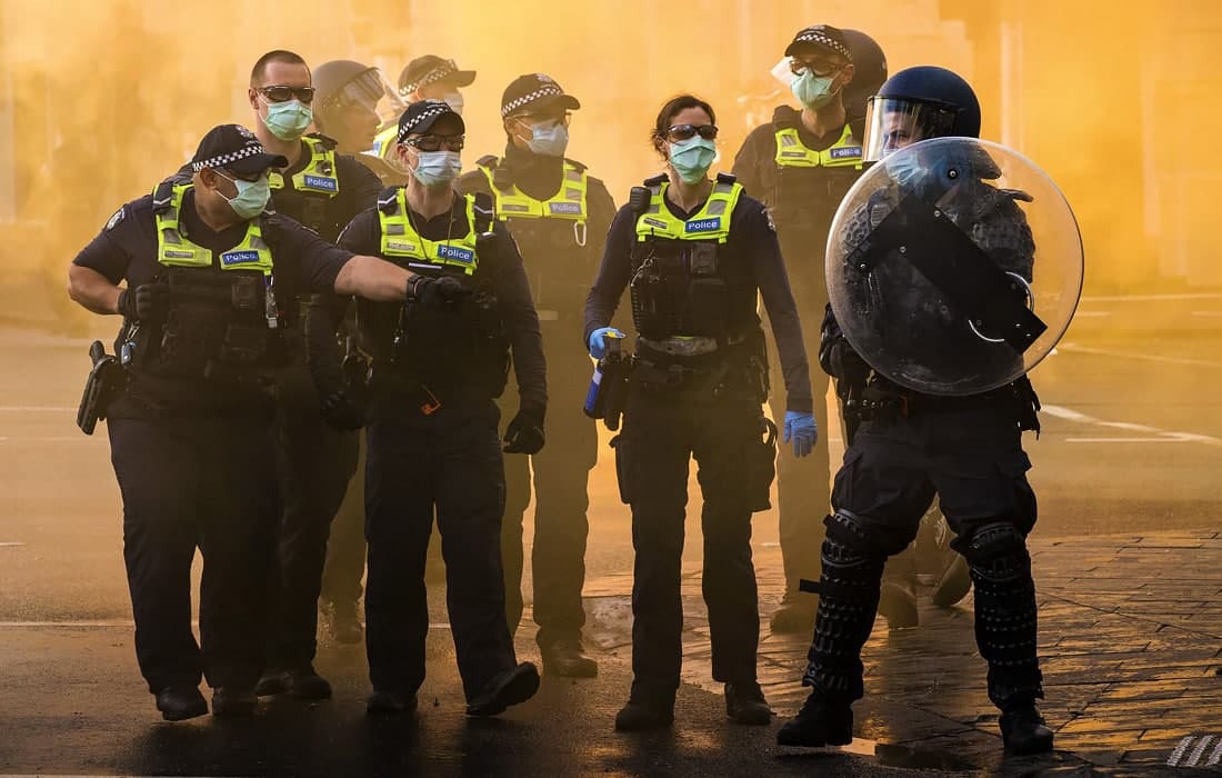Мелбурнда қурилиш ишчилари COVID-19 чекловларига норозилик билдираётган вақтда уларни назорат қилиб турган полиция ходимлари.
