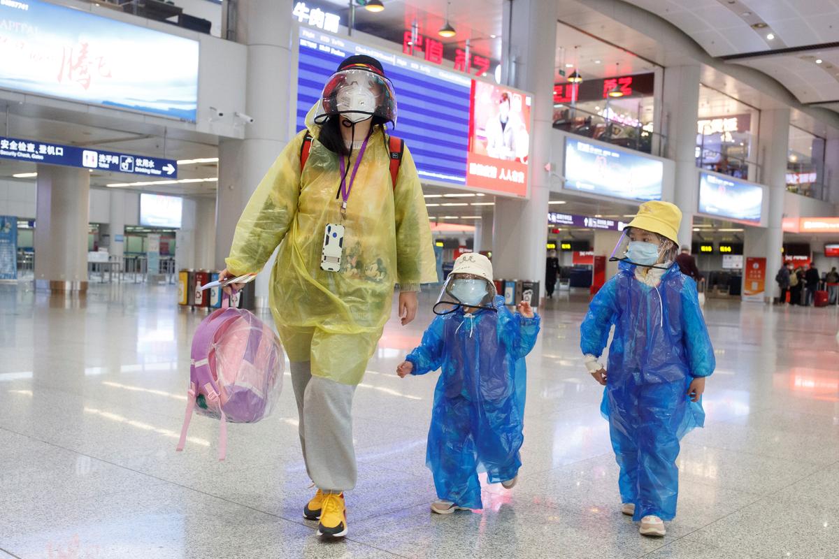 Пекин халқаро аэропортининг деярли бўш учиш залида коронавирусдан ҳимояланиш учун ниқоб тақиб, ёмғирпўш кийиб олган йўловчилар.