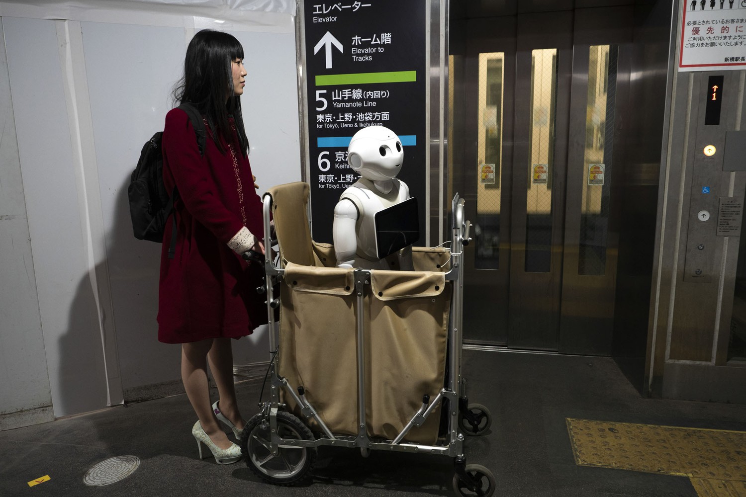 Токиодаги темир йўл станциясида роботни аравачада олиб кетаётган аёл лифт пойламоқда.