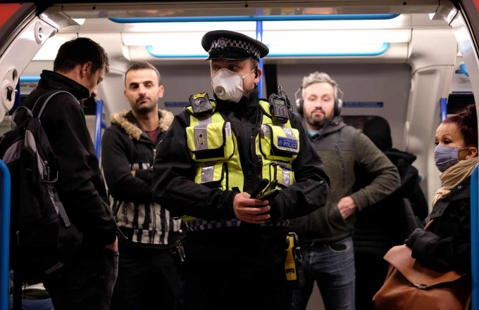 Londondagi metroda ertalabki tig‘iz vaqtda turgan politsiya xodimi va yo‘lovchilar.