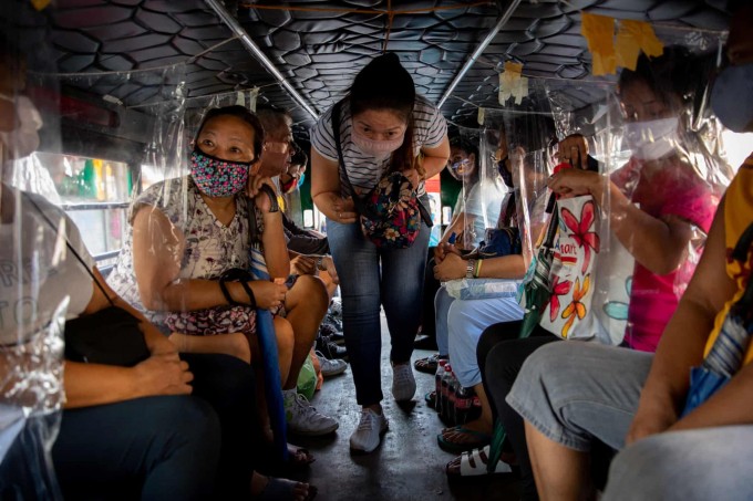 Filippinning Angono shahrida masofa saqlash uchun o‘rnatilgan qo‘lbola plastik to‘siqlarga ega transportda joyiga o‘tirayotgan yo‘lovchi.