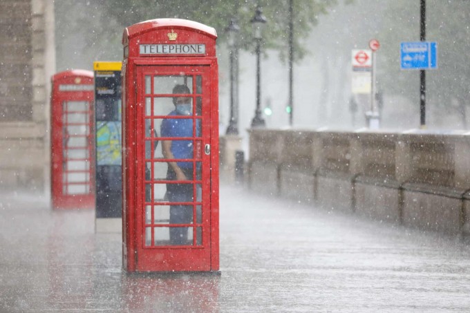 Buyuk Britaniyaning London shahrida kuchli yomg‘irdan telefon budkasida berkinib turgan erkak.