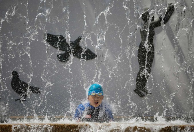 Yaponiyaning Tokio shahrida jamoat fontani ostida salqinlanib olayotgan bolakay.