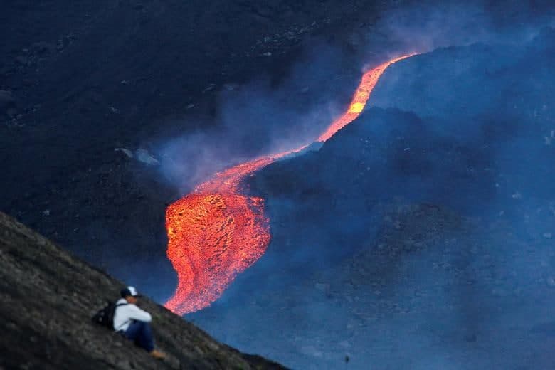 Gvatemaladagi Pakaya vulqonidan oqib tushayotgan lava manzarasi fonida o‘tirgan erkak.