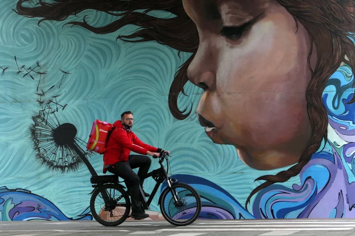 Belgraddagi Eski Sava ko‘prigi ostidagi devorga chizilgan graffiti yonidan velosipedda o‘tayotgan kishi.