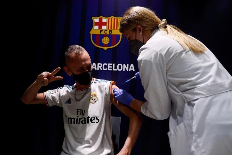 «Барселона» клубининг «Камп Ноу» стадионида «Реал Мадрид» жамоаси формасини кийган одам коронавирусга қарши Pfizer вакцинаси билан эмланмоқда.