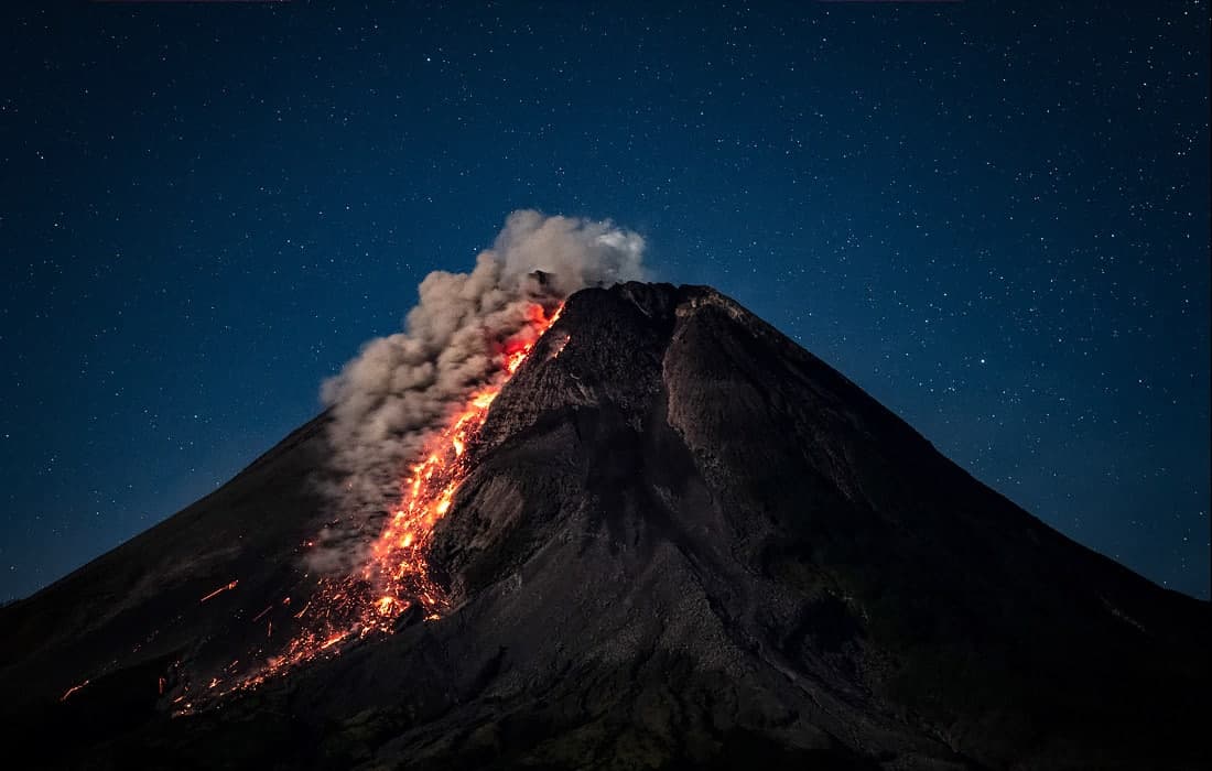 Yulduzlarga to‘la osmon fonida lava chiqarayotgan Indoneziyadagi Merapi vulqoni.