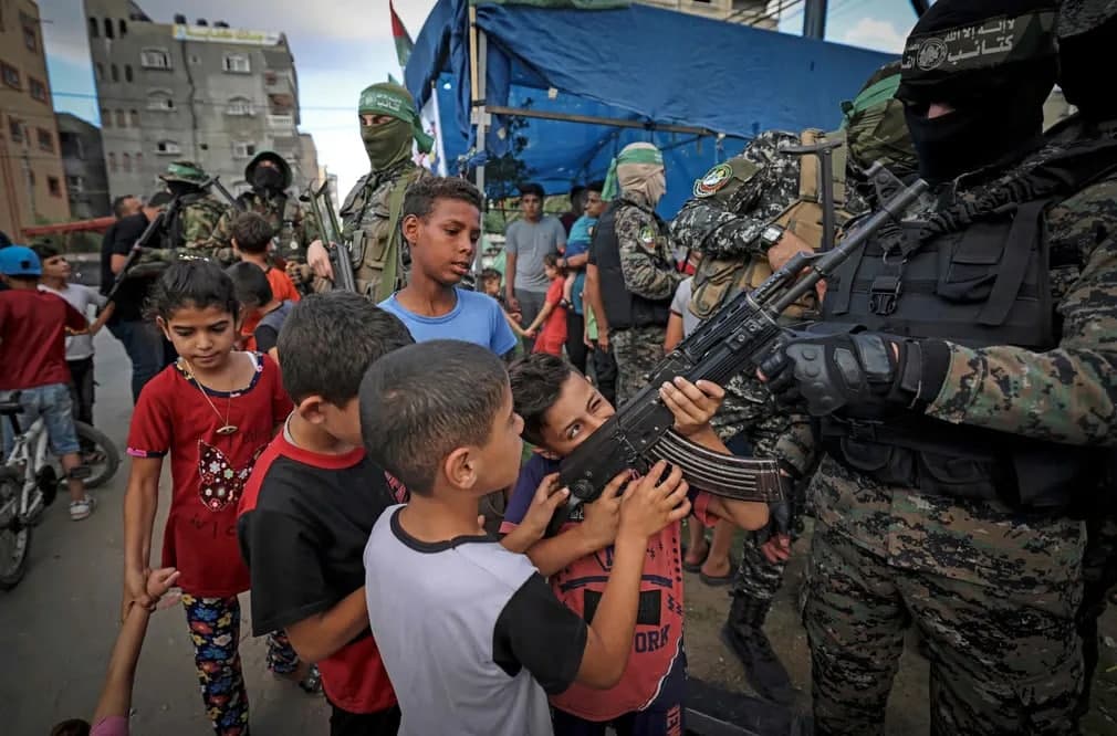 Falastinlik bolalar Izz ad-Din al-Qassam brigadasi a’zosiga tegishli qurolni ushlab turibdi.