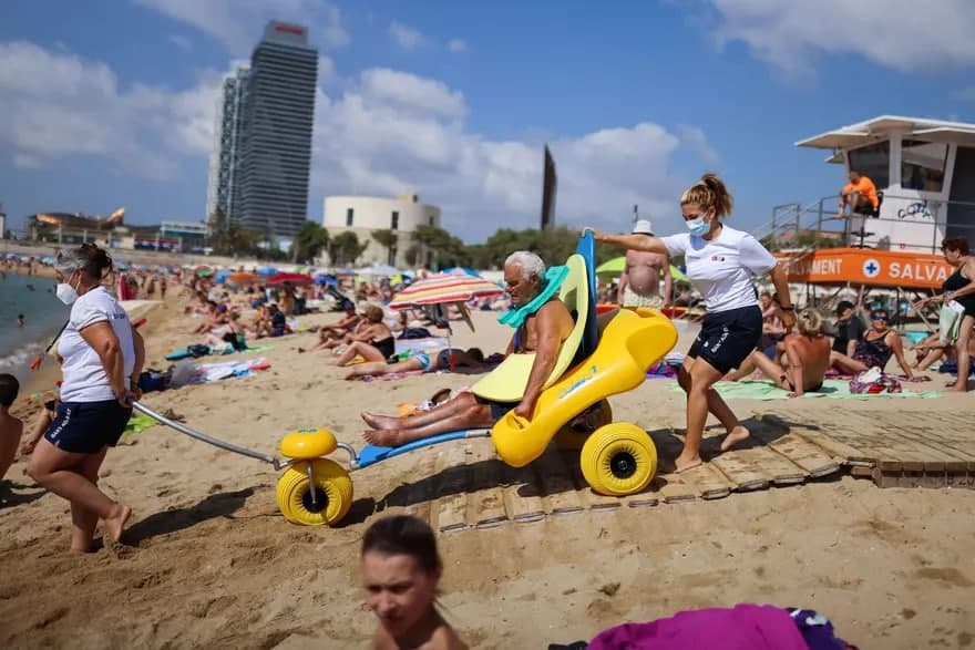 Барселона шаҳри соҳилида махсус пўкаклар кийиб олган 80 ёшли Мануэль Молина пляж ходимлари ёрдамида денгизга тушмоқда.