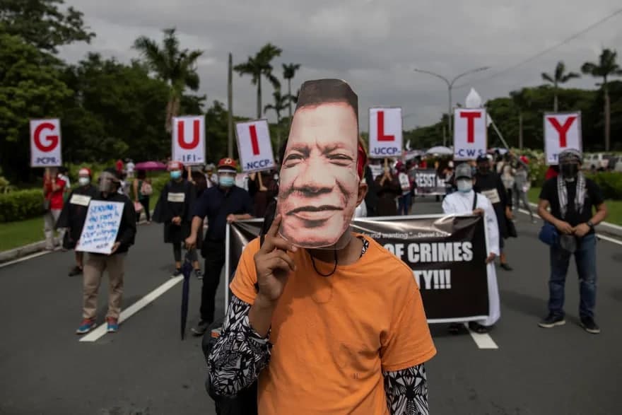 Filippin prezidenti Rodrigo Duterte niqobidagi namoyishchi uni insoniyatga qarshi jinoyatlarda ayblayotgan plakatlar oldida turib namoyishlarda qatnashmoqda.