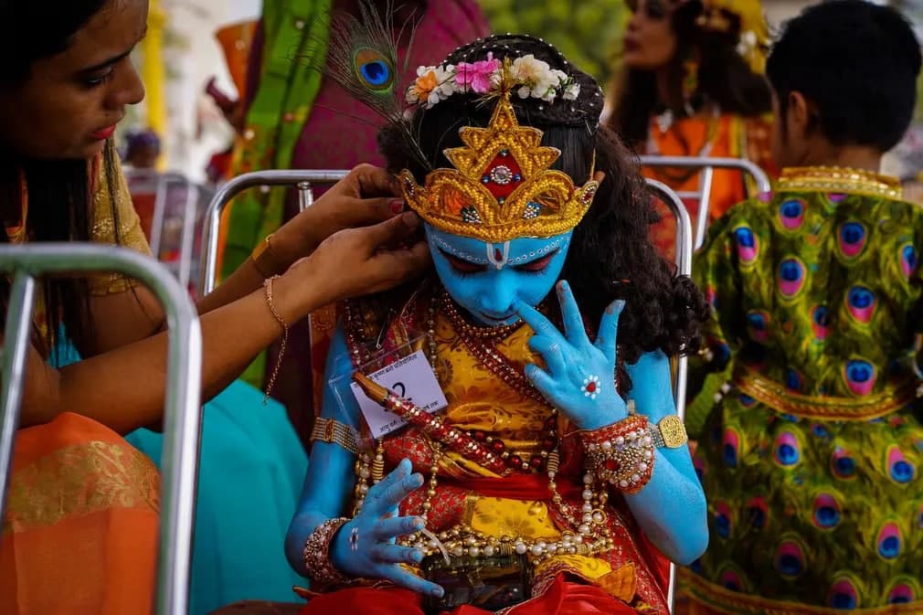 Hind xudosi Krishna kostyumidagi telefoniga tikilib o‘tirgan bolakayning kiyimidagi oxirgi tugmani qadayotgan ayol