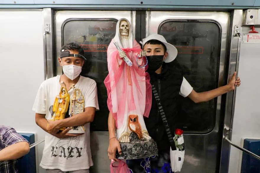 Meksikadagi metro vagonida Santa Muerte (Muqaddas o‘lim) haykallarini ko‘tarib turgan ikki yigit.