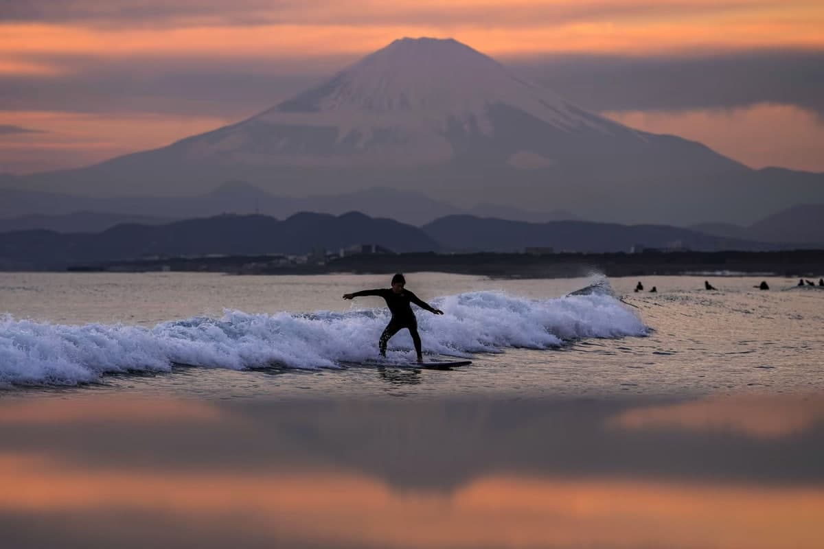 Япониянинг Токио жанубидаги Фудзияма вулқони фонида сёрфинг билан шуғулланаётган одам.