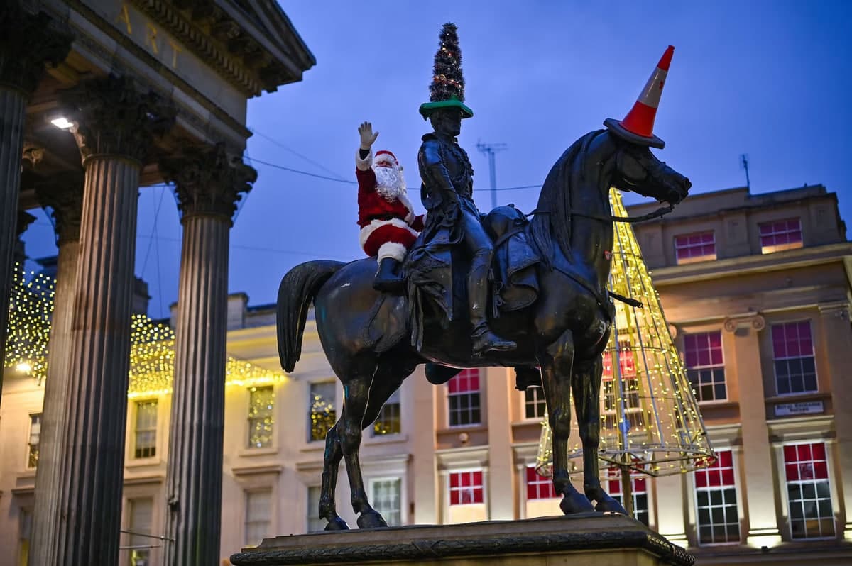 Шотландиянинг Глазго шаҳридаги Веллингтон герцоги ҳайкали тепасида Санта Клаус костюмини кийган эркак.