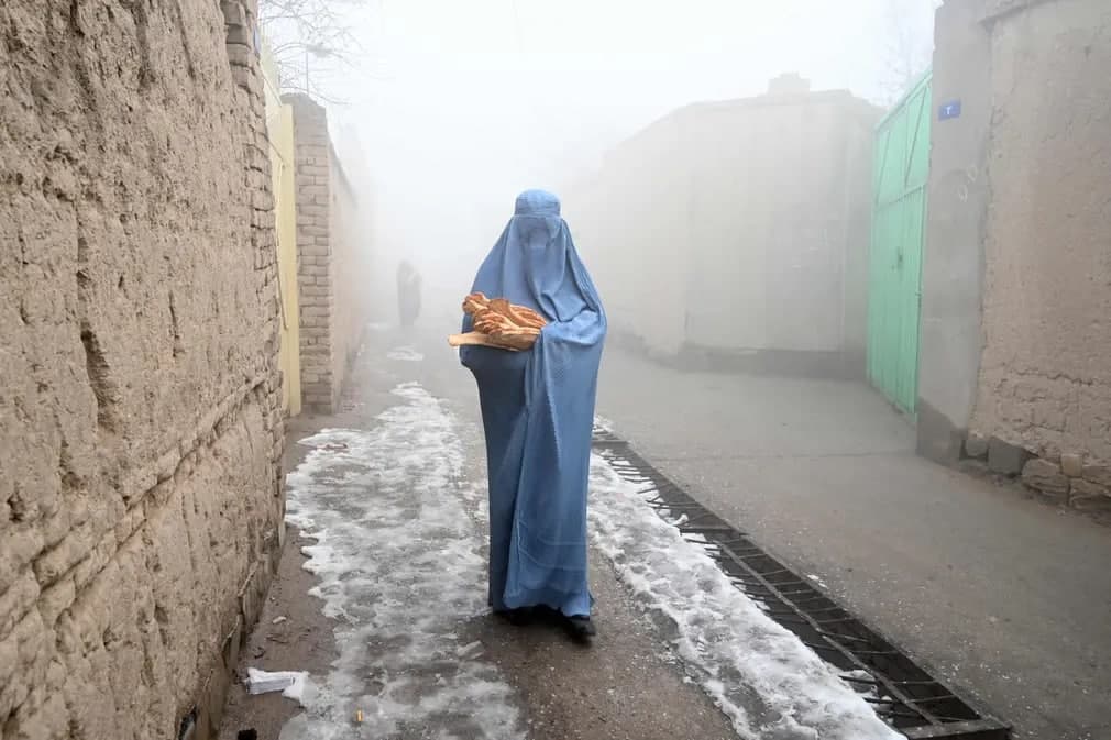 Burqa kiygan ayol Kobulda “Afg‘onlarni ochlikdan qutqar” kampaniyasi doirasida tarqatilgan tekin nonni olgach, uyi tomon yo‘l bo‘ylab ketmoqda.