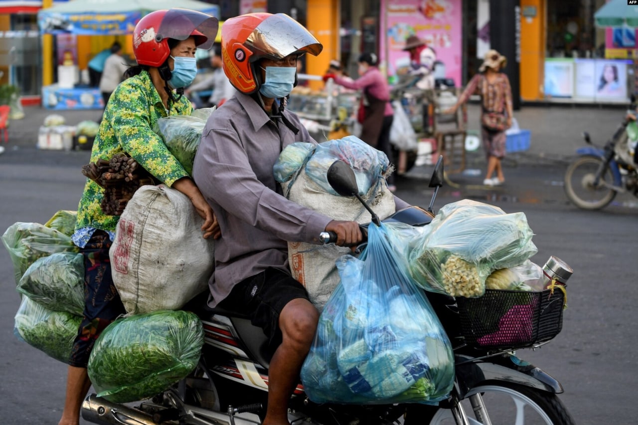 Kambojaning Pnompen shahrida mototsiklda sabzavot tashib ketayotgan er-xotin.