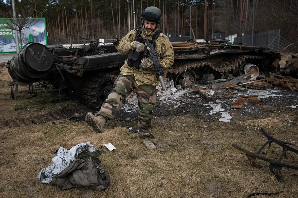 Ukraina askari kuygan to‘shak qoldig‘ini tepmoqda. Orqada yonib ketgan rus tanki. Avtoturargoh, Ukraina