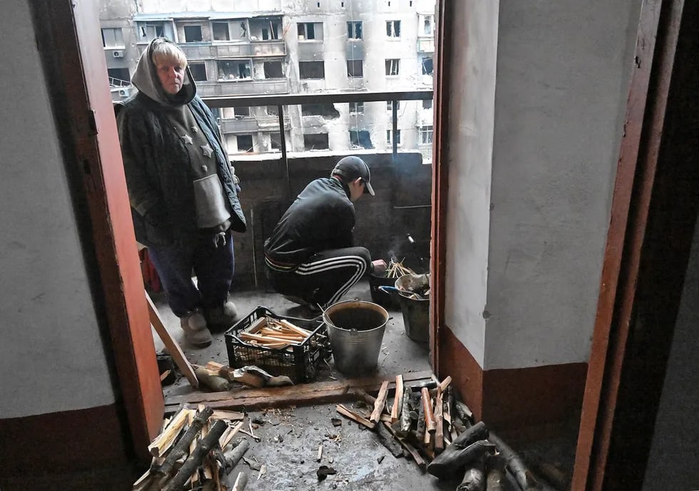 Mariupol aholisi shaharning Pravoberejniy tumanidagi zarar yetgan turar joy binosining balkonida olov yoqmoqda.