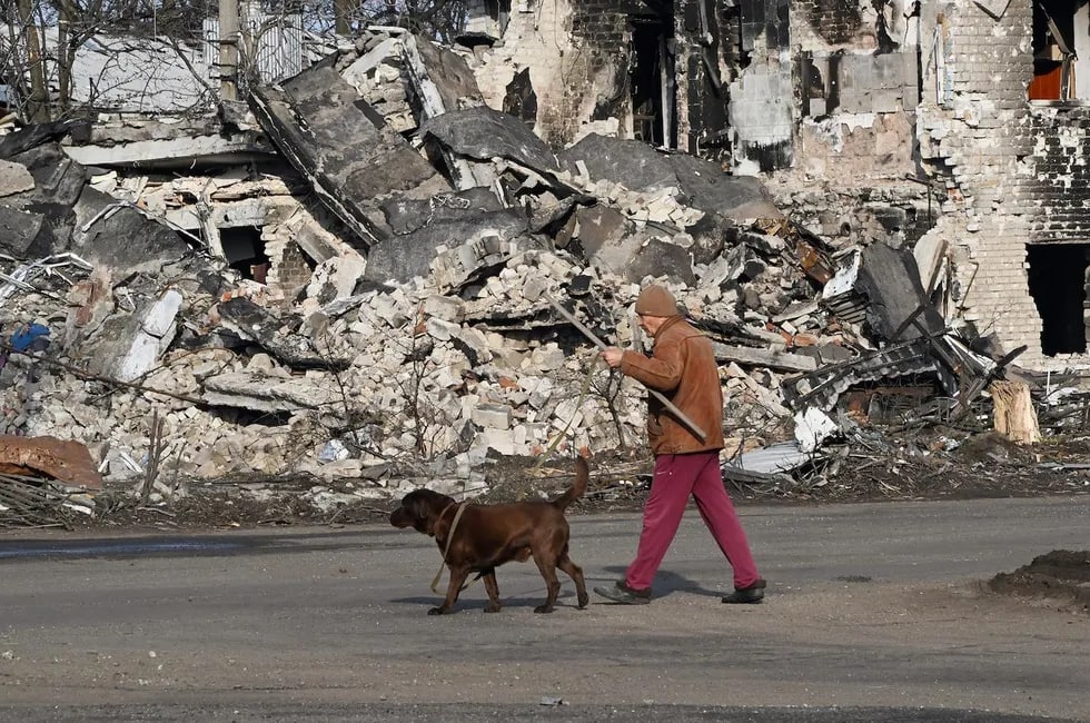 Vayron qilingan binolar orasida iti bilan ketayotgan mahalliy aholi vakili. Volnovaxa, Donetsk viloyati.