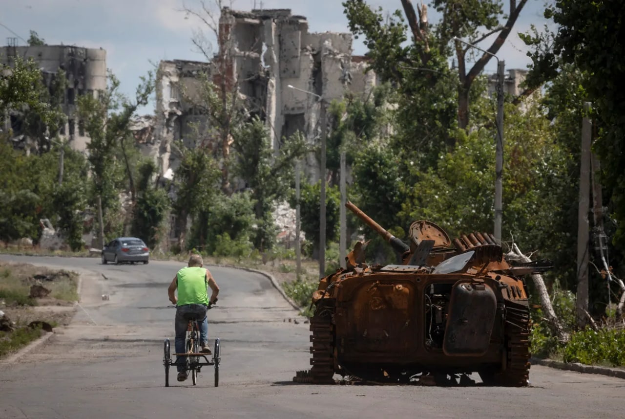 Lugansk viloyatining Rubejnoye shahri ko‘chasida yonib ketgan tank yonidan velosipedda o‘tayotgan kishi. Rubejnoye Rossiya qurolli kuchlari tomonidan egallangan, ular iyun oyi oxirida ushbu shaharni ham o‘z ichiga oluvchi aglomeratsiyaga kirdi.