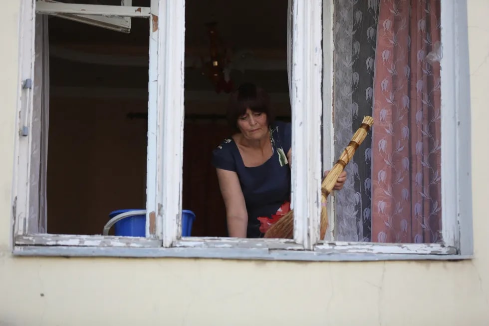 Donetskdagi zarar yetgan turar joy kvartalida derazasi oldini tozalayotgan ayol. Shaharda DXR ma’muriyati joylashgan bino, jurnalistlar yashayotgan “Markaziy” mehmonxonasi va ko‘p qavatli uy o‘qqa tutilgan.