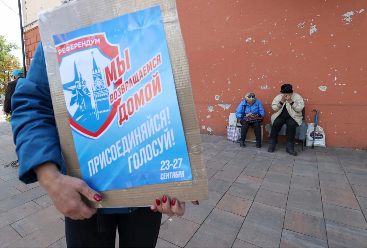 Mariupolda ayol o‘zini o‘zi respublika deb e’lon qilgan DXRning Rossiyaga kirishi bo‘yicha “referendum” plakatini ko‘tarib kelmoqda.