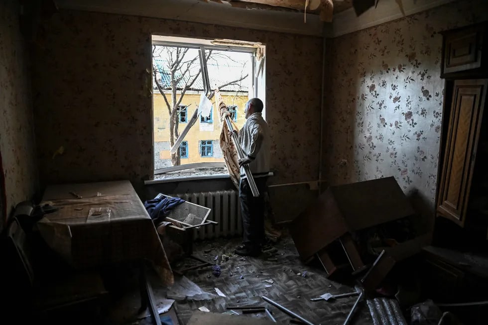 Украина назоратидаги Краматорскда яшовчи киши Россия ҳужумидан вайрон бўлган квартирасини тозаламоқда.