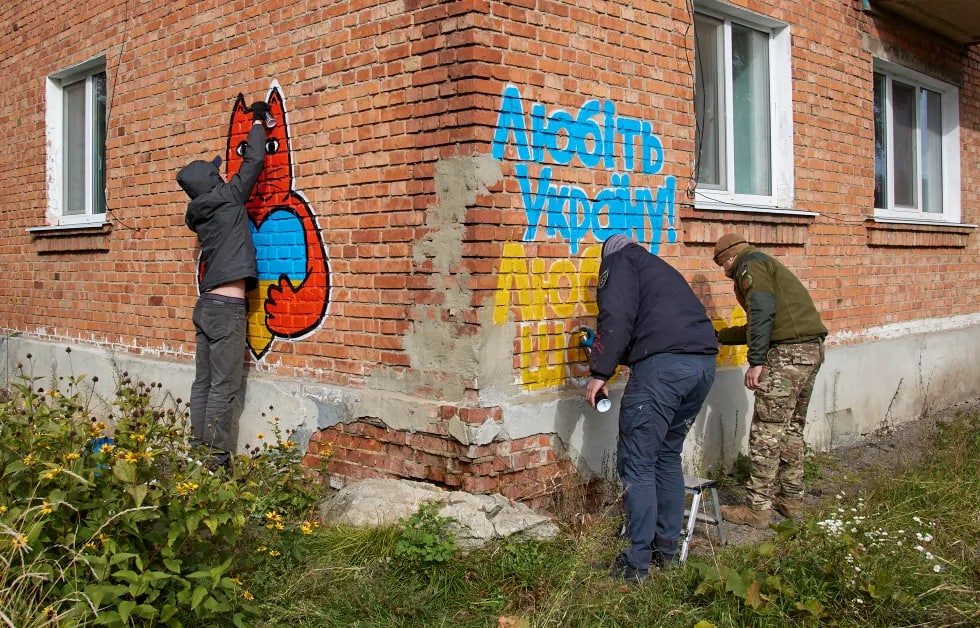 Кўча рассомлари Купянскдаги уй деворига Украина байроғи рангларида граффити чизмоқда.