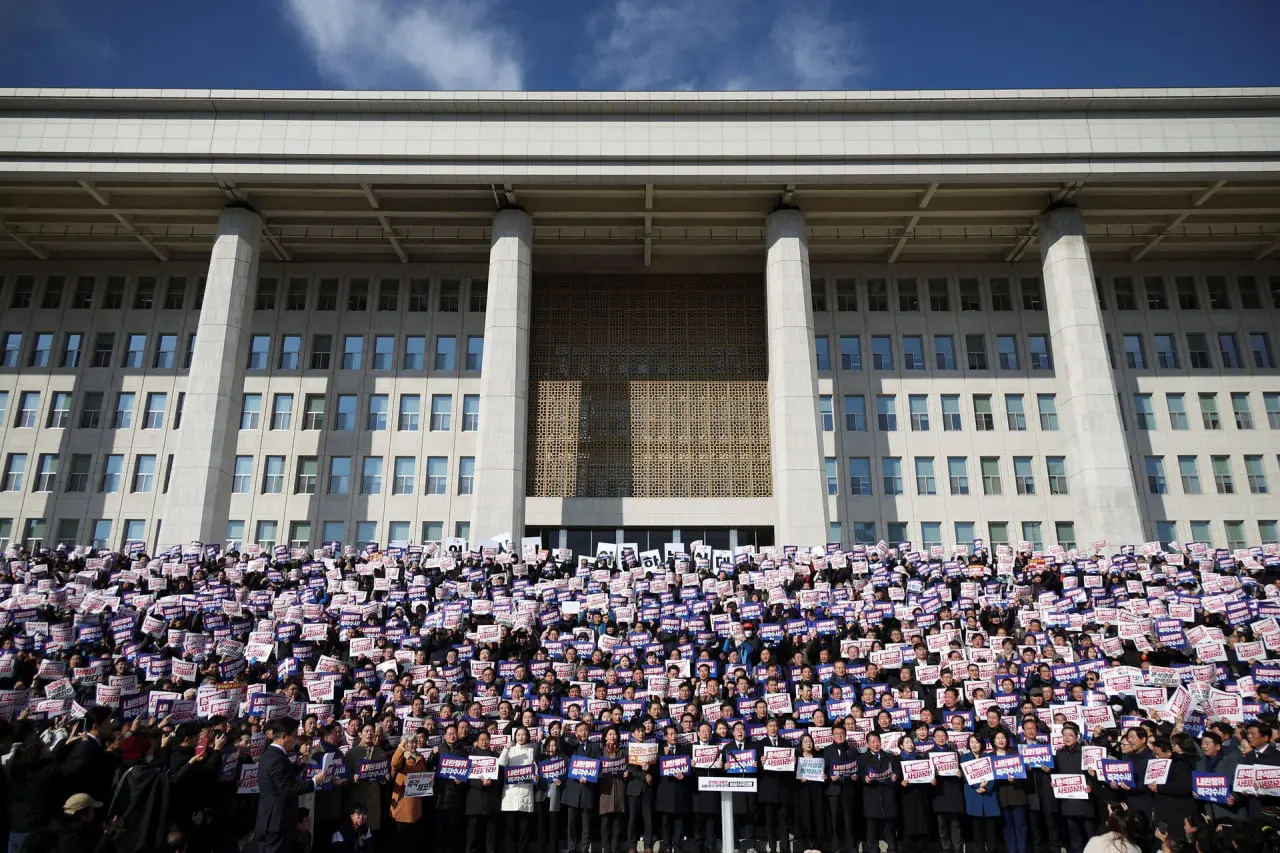 Протестующие держат плакаты, пока люди и законодатели присутствуют на митинге, осуждающем неожиданное объявление президентом Южной Кореи военного положения